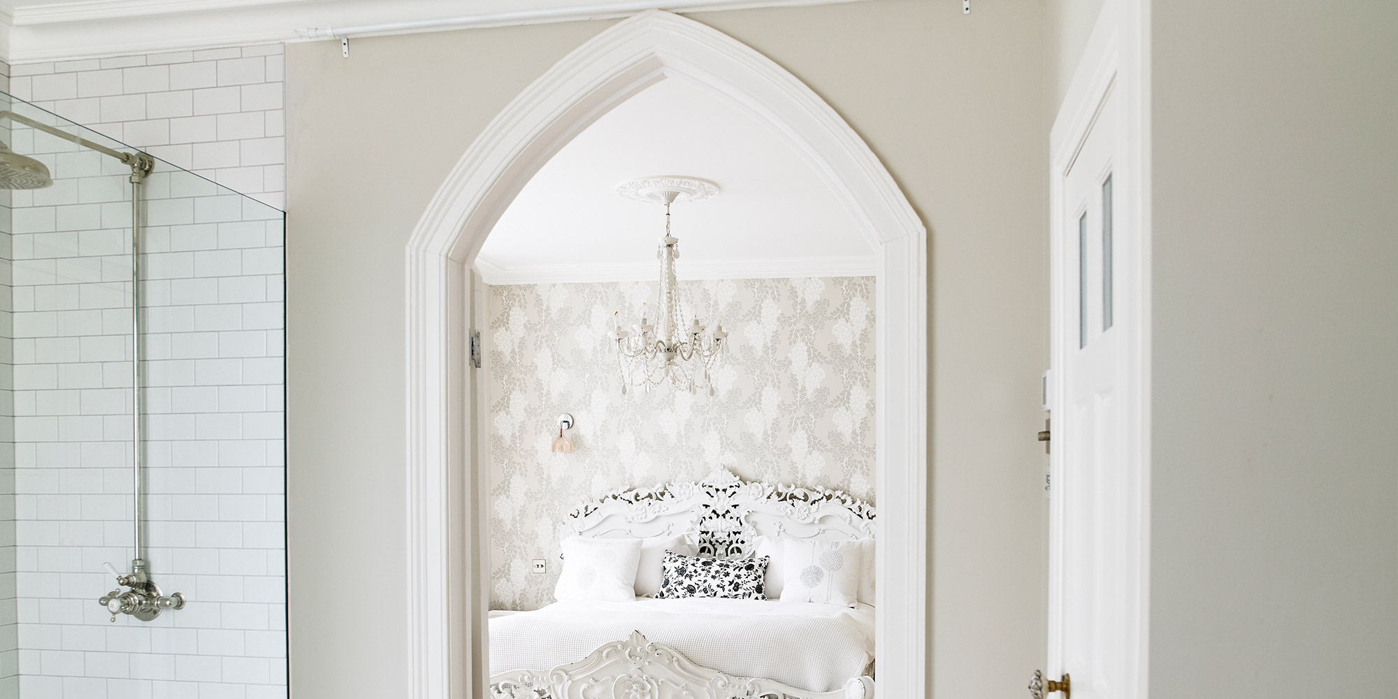 Blick durch eine weiße Türzarge in ein Schlafzimmer mit Kronleuchter und Ornamentbett