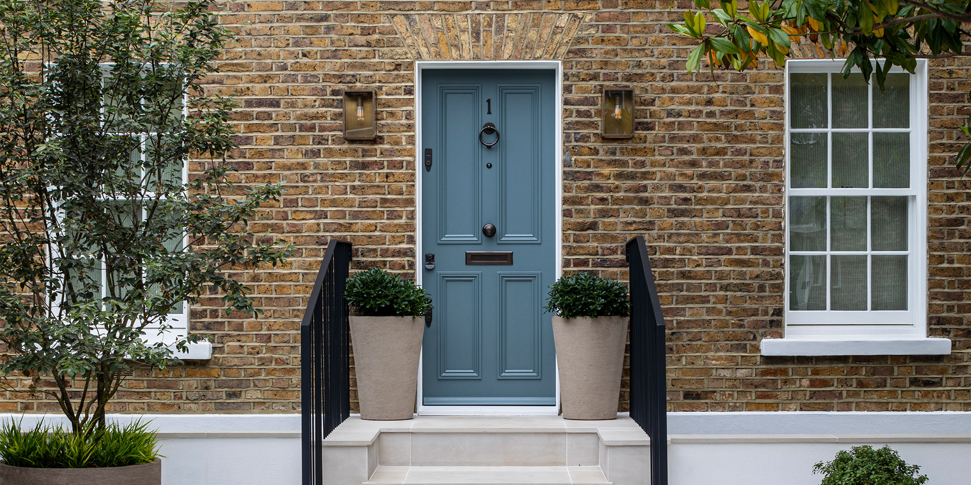 Blaue Haustür in Backsteinfassade mit zwei Pflanzkübeln am Eingang