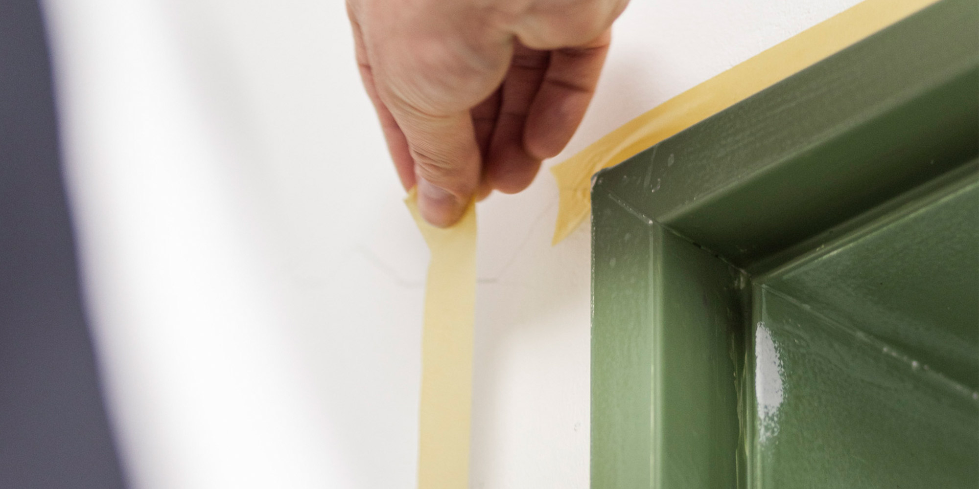 Hand klebt Abdeckband an eine Kante fuer saubere Farblinien