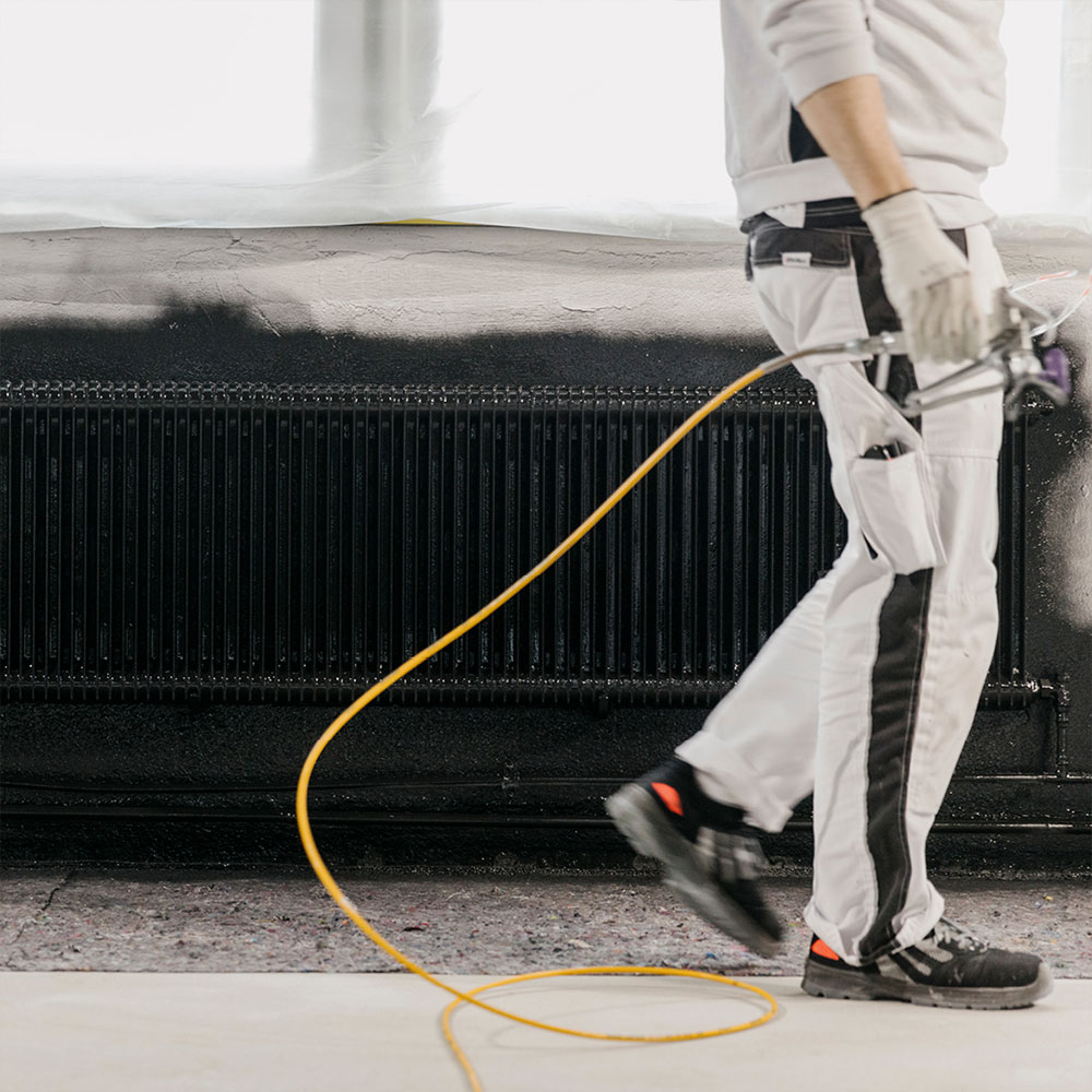 Heizkoerper wird mit Spruehgeraet schwarz lackiert - gleichmaessiger Auftrag beim Heizkoerper streichen